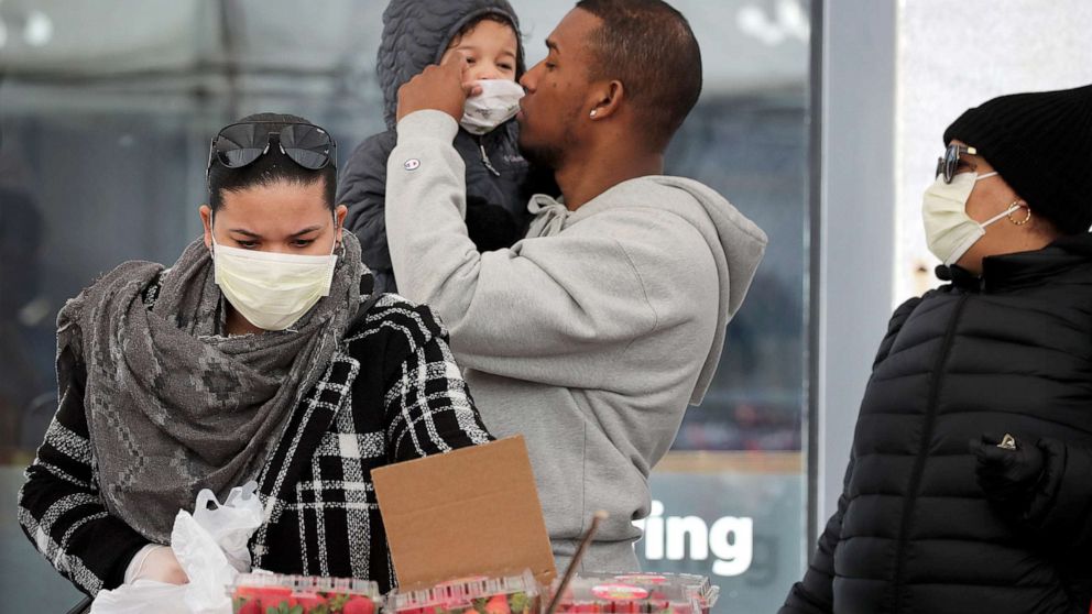 PHOTO: A man carries his daughter while the family shops for produce at Haymarket in Boston, Mass., March 13, 2020. The family said they were wearing masks out of precaution due to the coronavirus.