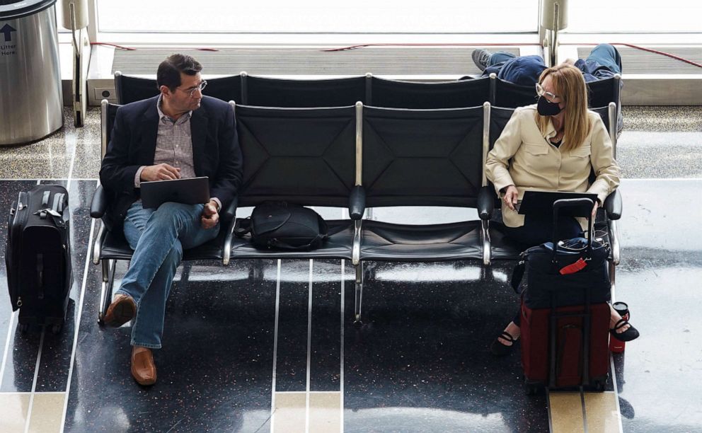 PHOTO: Airline passengers, one unmasked and one wearing a face mask, await their flight after a federal judge's ruling that mask mandate on public transportation was unlawful, at Ronald Reagan Washington National Airport in Arlington, Va., April 19, 2022.