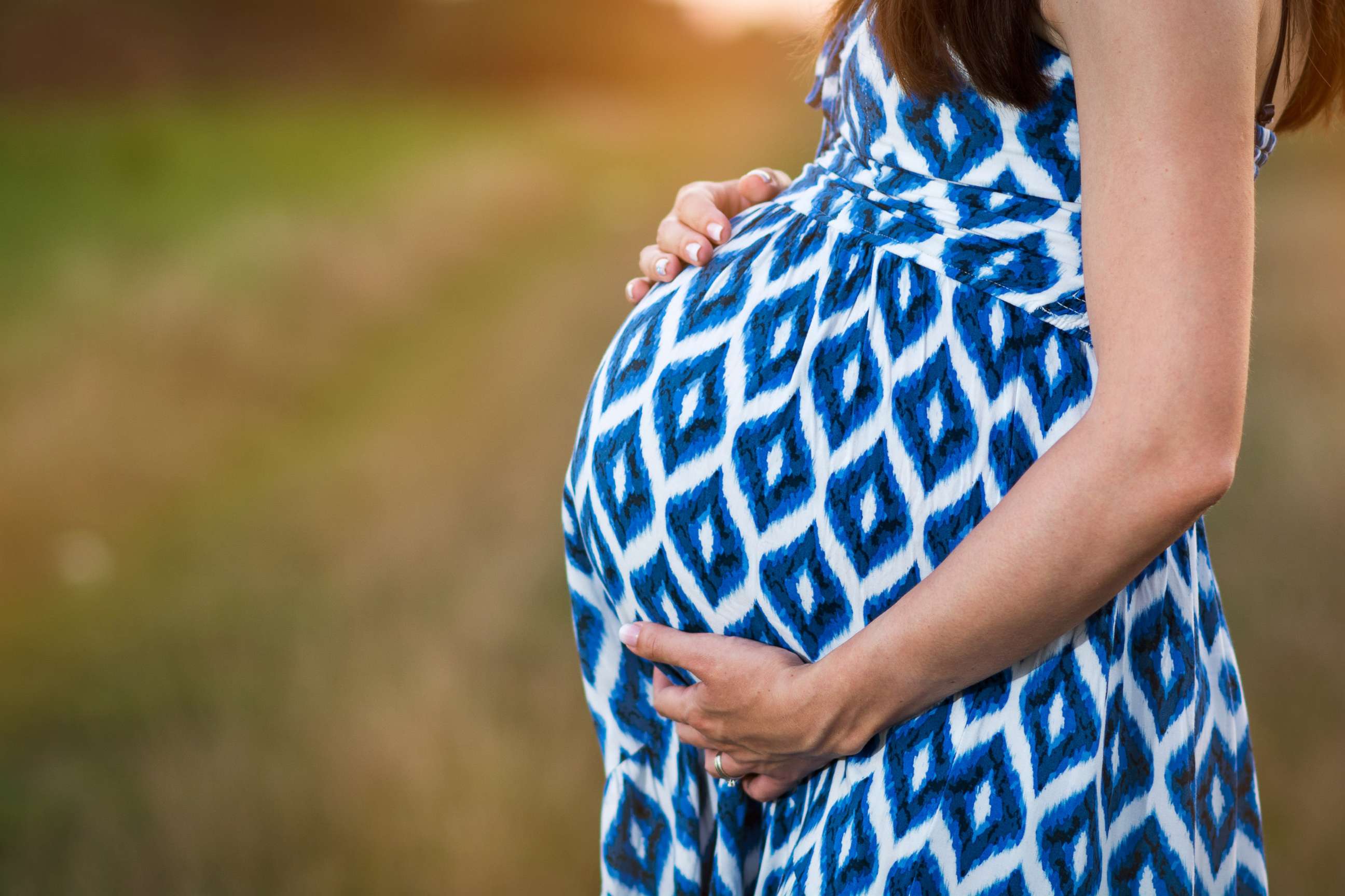 PHOTO: A pregnant woman poses in blue dress cradling her belly in this stock image. 