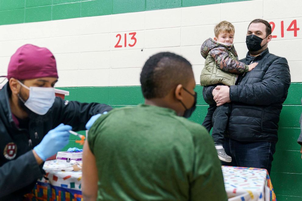 PHOTO: Brian Stachowiak, right, holds his son, Noah, 5, as he watches another child receive a Covid-19 vaccination, while waiting his turn at Nathanael Greene Elementary School in Pawtucket, R.I., Dec. 7, 2021. 