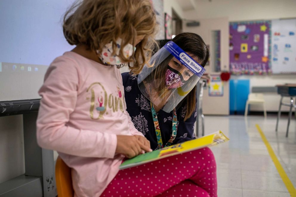 PHOTO: Teacher Elizabeth DeSantis, wearing a mask and face shield, listens as a first grader reads during class at Stark Elementary School on Sept. 16, 2020 in Stamford, Conn.