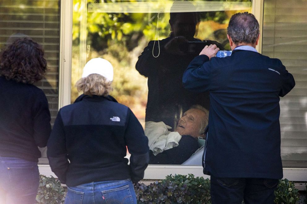 PHOTO: In this March 18, 2020, file photo, Chuck Sedlacek, a patient at the Life Care Center, smiles through a window at his children Seri Sedlacek (L), Susan Sedlacek and Scott Sedlacek (R) who have come to visit him in Kirkland, Wash.