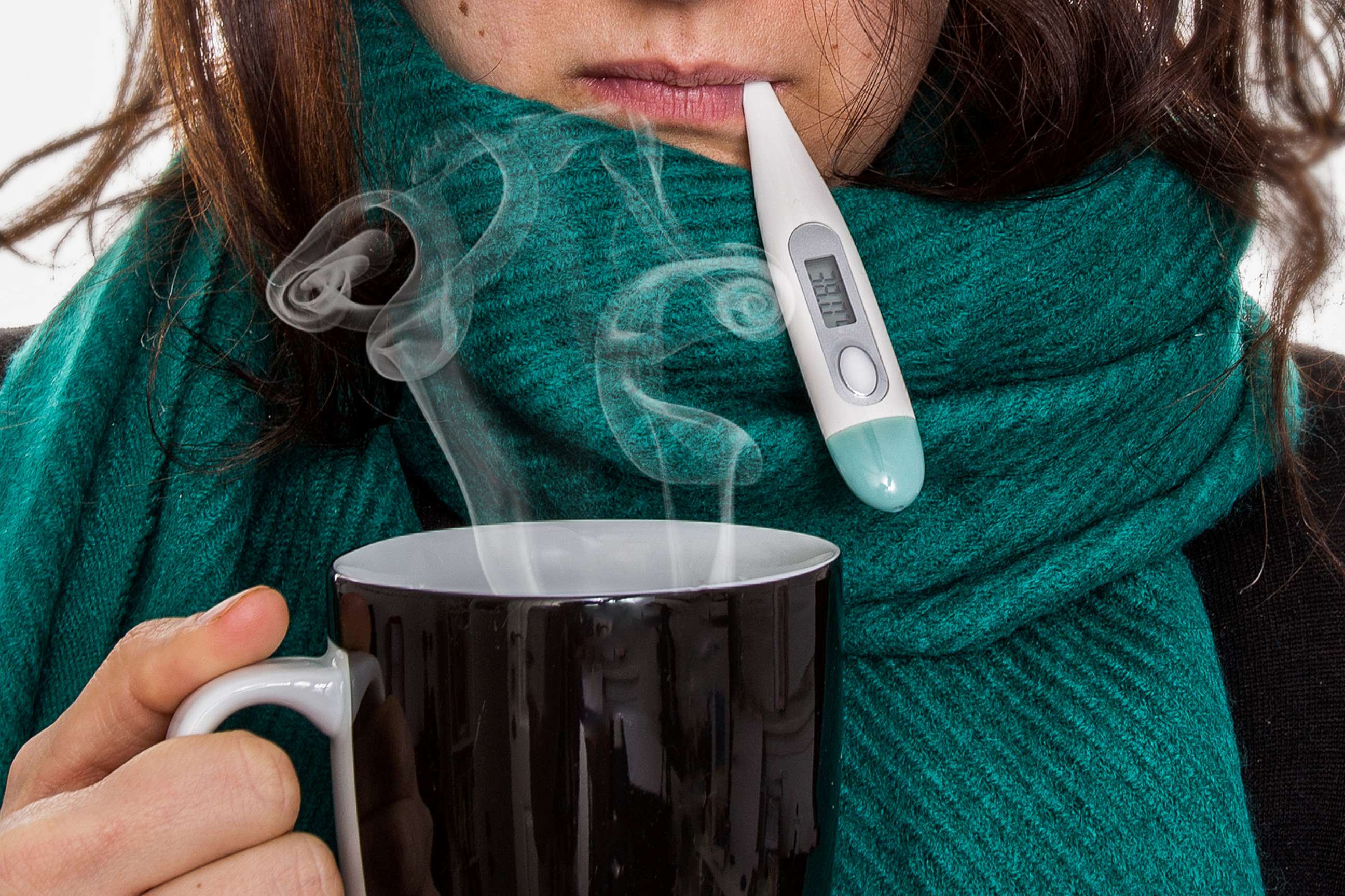 PHOTO: A stock photo of a woman taking her temperature and drinking a warm beverage.