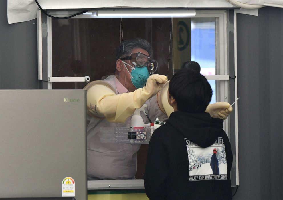 PHOTO: A medical staff member in a booth takes samples from a visitor for the COVID-19 coronavirus test at a walk-thru testing station set up at Jamsil Sports Complex in Seoul on April 3, 2020. 
