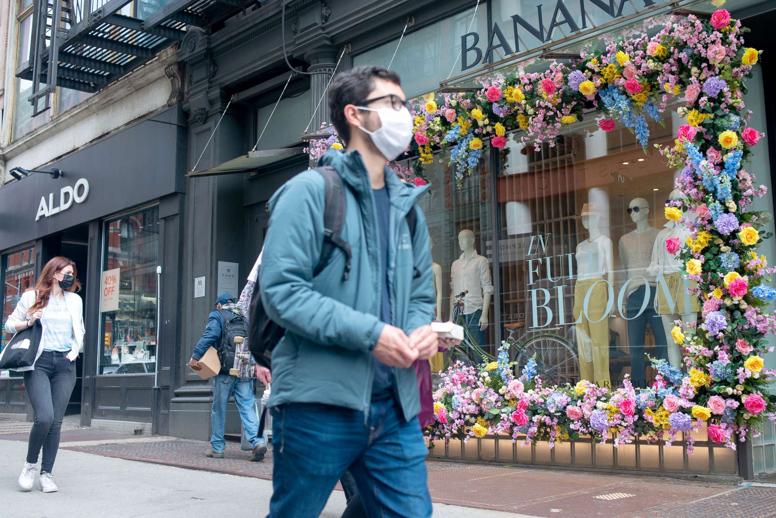 PHOTO: Pedestrians wear masks as they walk past a flower decoration at Banana Republic in the SoHo neighborhood of New York, March 25, 2021.