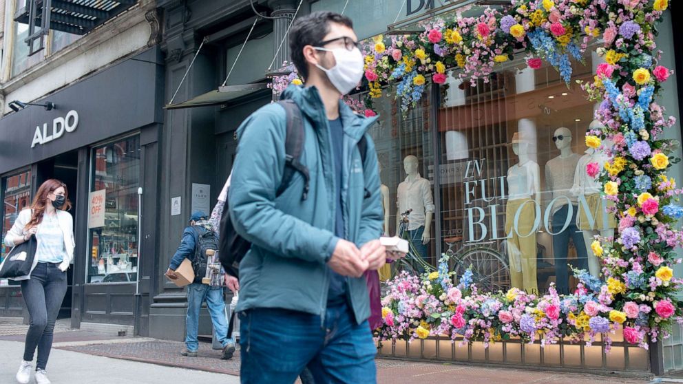 PHOTO: Pedestrians wear masks as they walk past a flower decoration at Banana Republic in the SoHo neighborhood of New York, March 25, 2021.