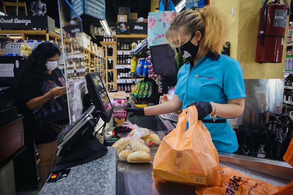 PHOTO: An employee at wears a protective face mask and gloves while ringing up a customer at a supermarket in Miami, Florida, July 8, 2020.