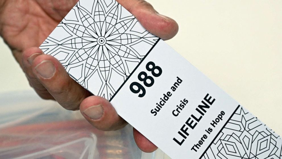 PHOTO: A bookmark for children with the 988 suicide and crisis lifeline emergency telephone number is displayed by Lance Neiberger while they speak about mental health and suicide awareness in Casper, Wy., Aug. 14, 2022.