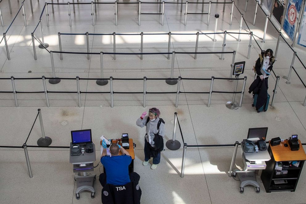 PHOTO: A passenger removes her goggles and face mask used to fend off coronavirus at the request of a TSA agent as she goes through a security checkpoint, March 24, 2020, at JFK airport in New York. 