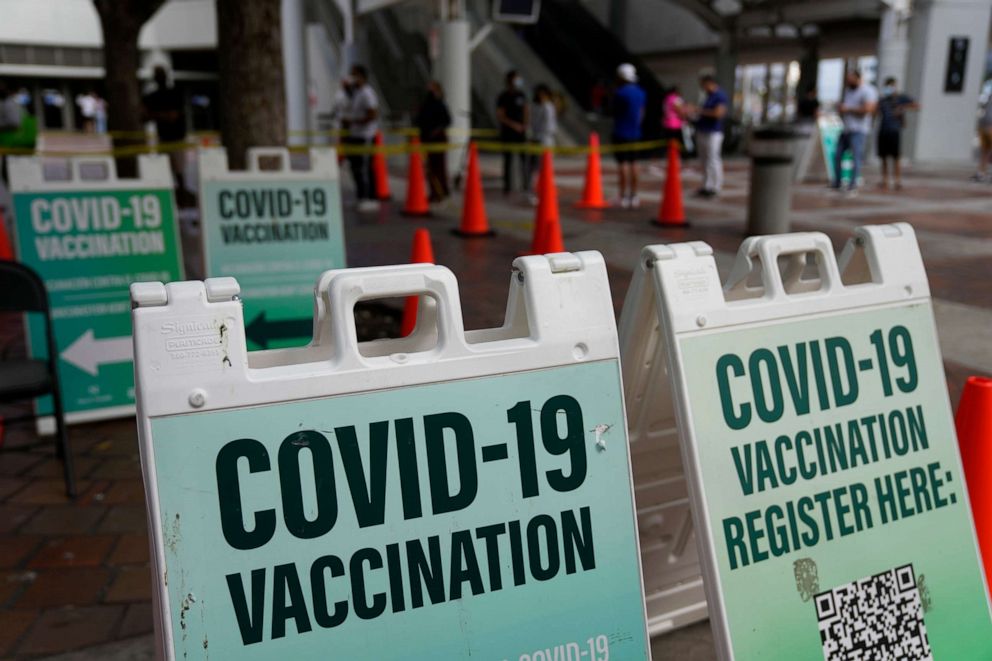 PHOTO: People wait in a distanced line to be tested for COVID-19, as signs point to other tents with no line where healthcare workers waited to administer vaccines, at a mobile health unit run by Nomi Health, Dec. 28, 2021, in Miami.