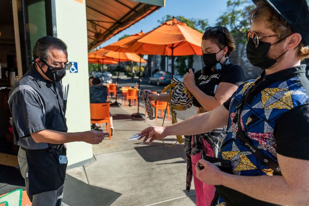 PHOTO: Waiter Juan Rodrigues, left, asks patrons to show their vaccination cards before entering the Fred 62 restaurant in Los Angeles, Nov. 29, 2021.