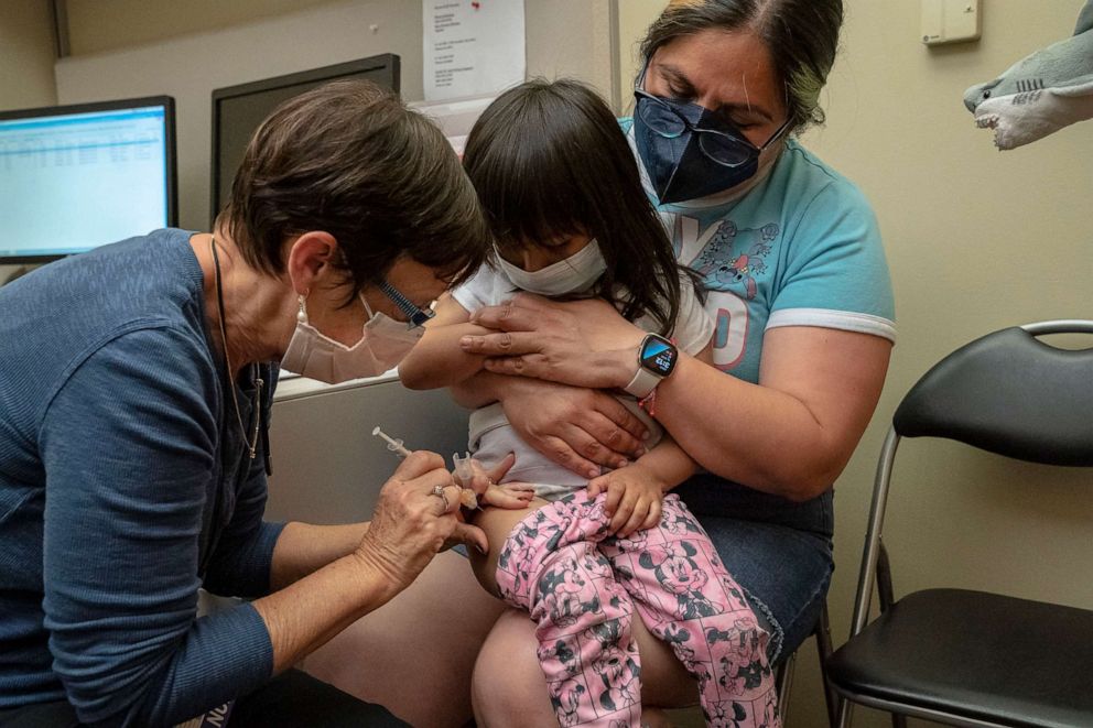 फोटो: 2 साल की डेनी वालेंज़ुएला ने फाइजर कोविड -19 टीकाकरण की अपनी पहली खुराक नर्स डेबोरा सैम्पसन से प्राप्त की, जबकि यूडब्ल्यू मेडिकल सेंटर - रूजवेल्ट, 21 जून, 2022 को सिएटल में उसकी मां शीहुइटल मेंडोज़ा द्वारा आयोजित की जा रही थी।