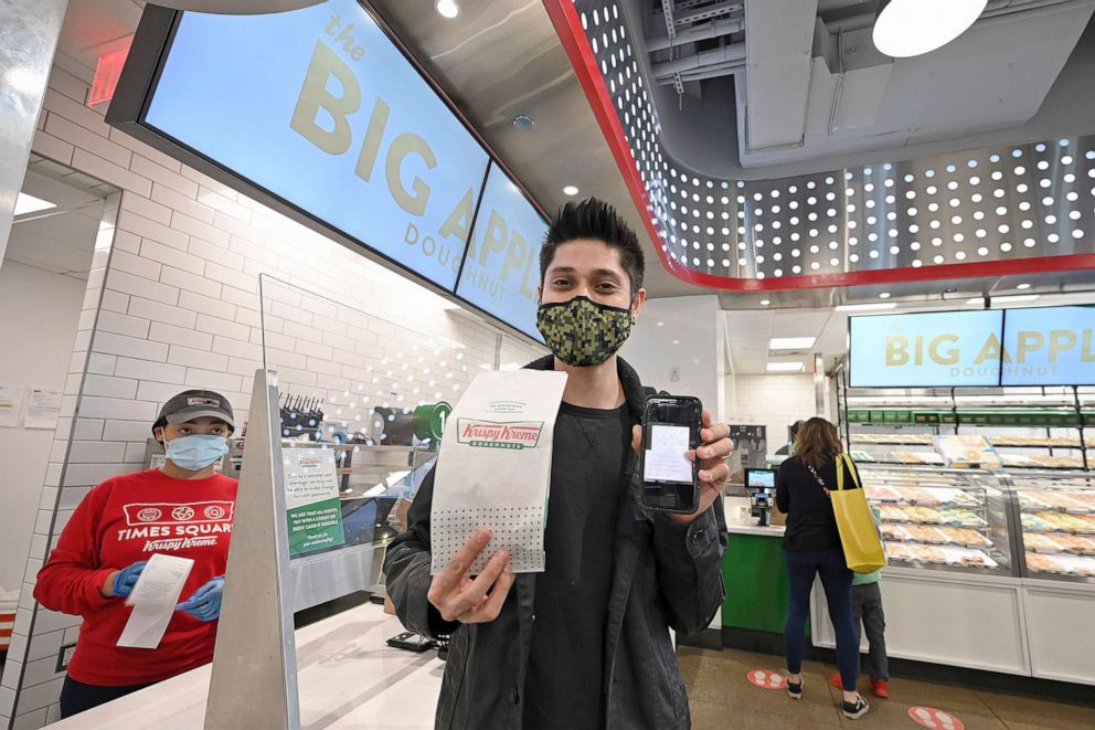 PPHOTO: Eddie Lopez shows an image of his COVID-19 vaccination card after receiving a free Krispy Kreme doughnut in New York, NY, March 30, 2021. As part of a promotion, customers can receive a free original glazed donut by showing their vaccination card.