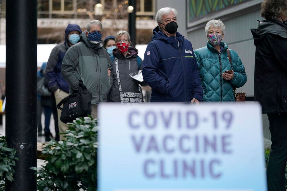 PHOTO: People stand near a sign as they wait in line to receive the first of two doses of the Pfizer vaccine for COVID-19, at a one-day vaccination clinic set up in an Amazon.com facility in Seattle, Jan. 24, 2021.