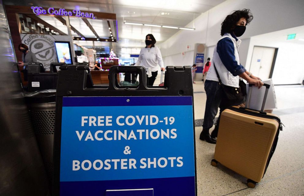 PHOTO: Travelers walk past a sign offering free COVID-19 vaccinations and booster shots at a pop-up clinic in the international arrivals area of Los Angeles International Airport in Los Angeles, Calif., Dec. 22, 2021.