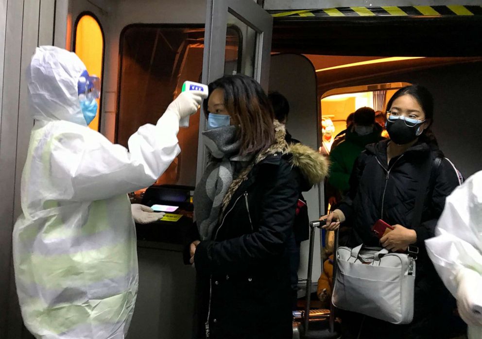 PHOTO: Health Officials in hazmat suits check body temperatures of passengers arriving from the city of Wuhan, Jan. 22, 2020, at the airport in Beijing, China. 