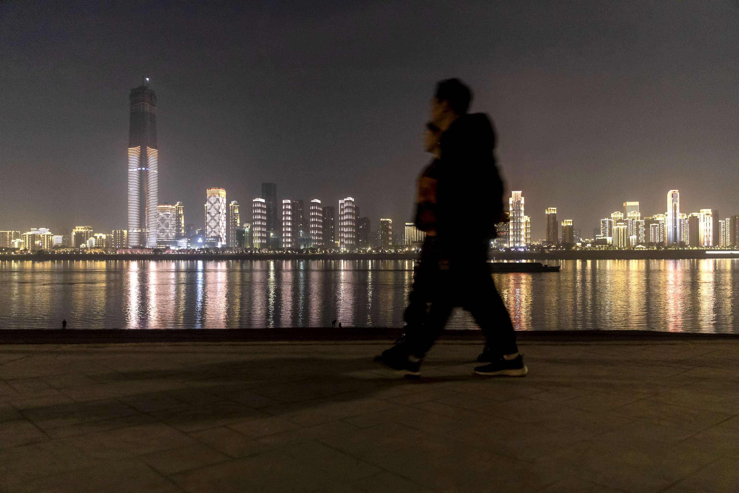 PHOTO: Pedestrians walks in front of illuminated buildings on the other side of the Yangtze River at night in Wuhan, Hubei, China, Dec. 9, 2019.