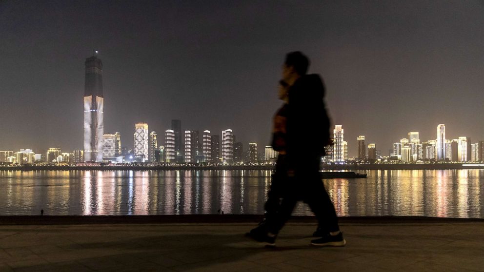 PHOTO: Pedestrians walks in front of illuminated buildings on the other side of the Yangtze River at night in Wuhan, Hubei, China, Dec. 9, 2019.