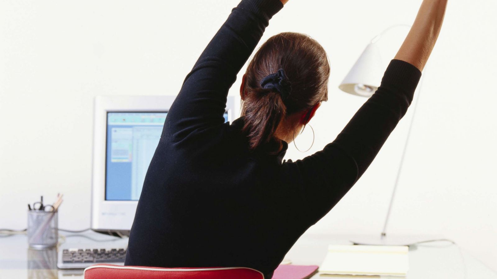 PHOTO: A young woman stretches at her desk in an undated stock photo.