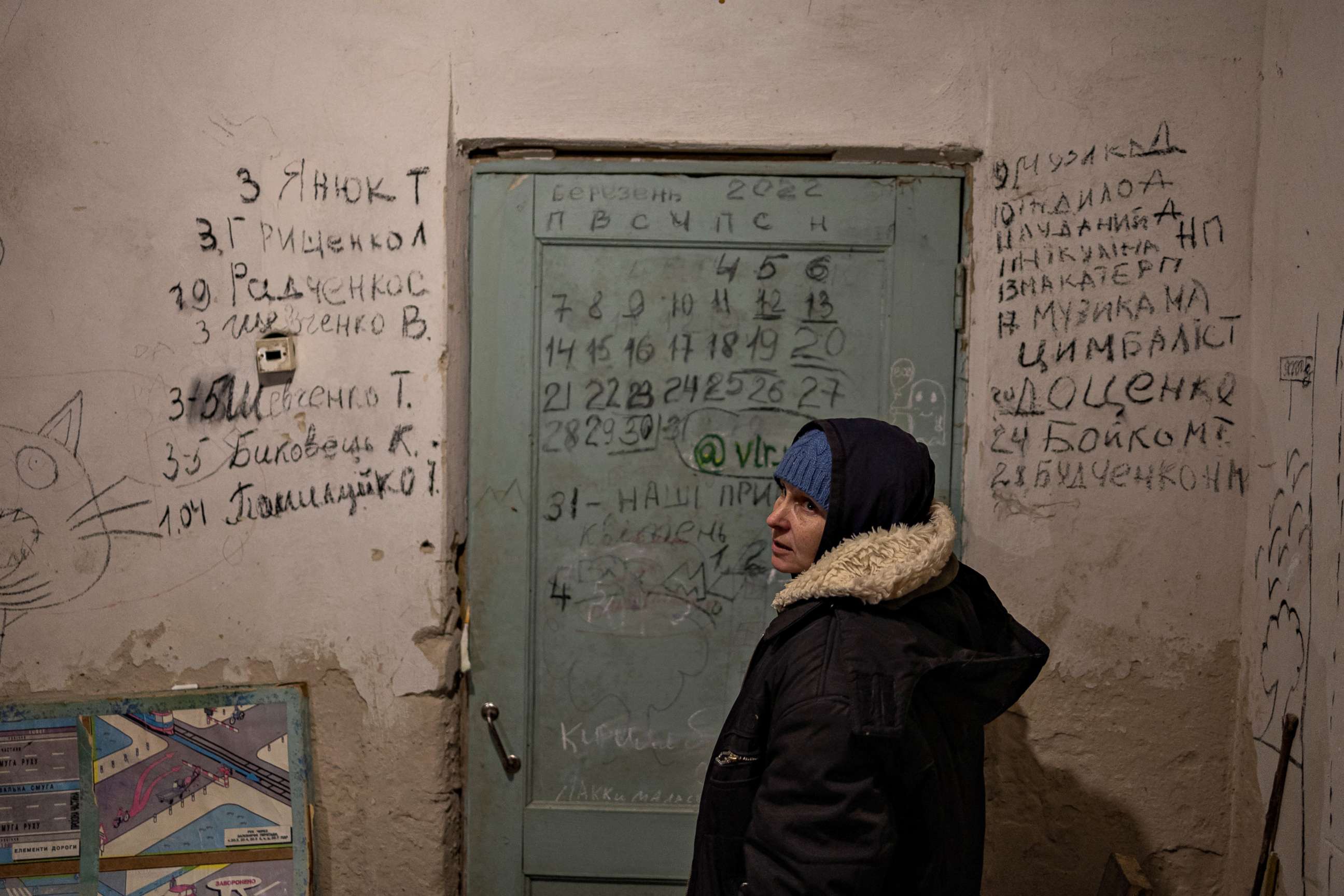 PHOTO: Halyna Tolochina stands in front of a wall inscribed with the names of people who died inside the school basement in Yahidne.