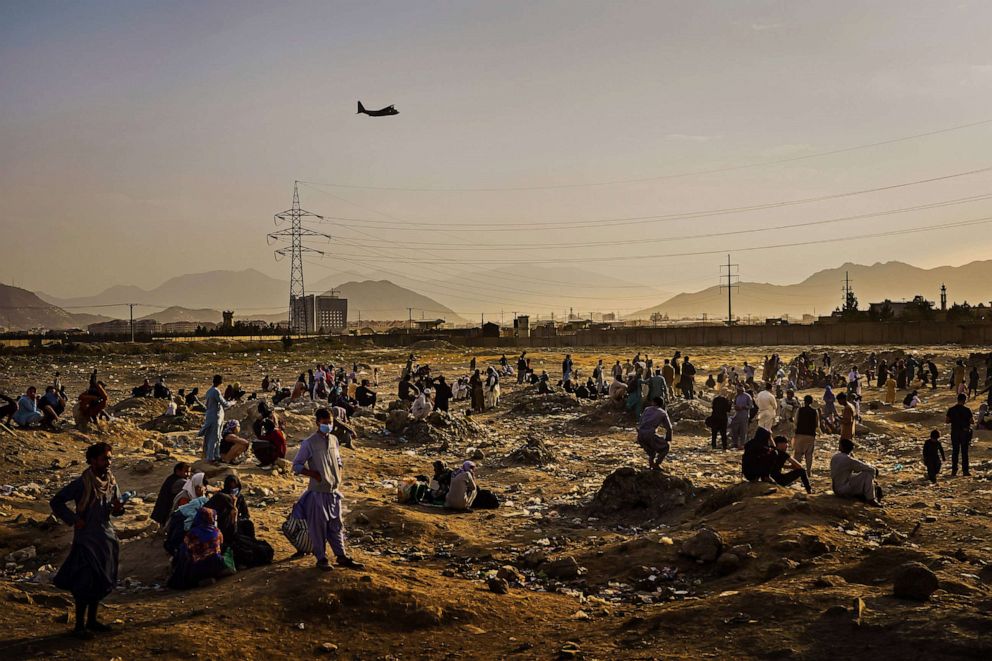 PHOTO: A military transport plane departs overhead as Afghans hoping to leave the country wait outside the Kabul airport on Aug. 23, 2021.