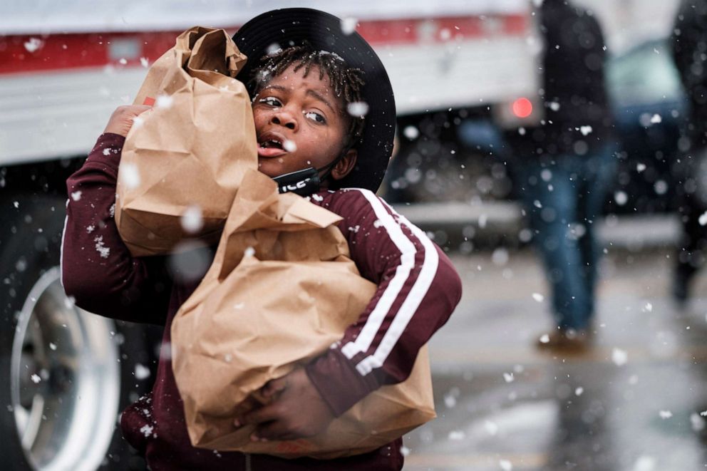 PHOTO: A child volunteering at a food distribution carries bags of food to people in line during a Thanksgiving food distribution at a park in Des Moines, Iowa during a snowstorm, Nov. 23, 2020.