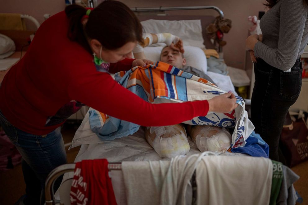 PHOTO: Lidiya Gladun checks the bandages on her son's severed legs at the hospital in Cherkasy, Ukraine, May 6, 2022. 22-year-old Anton Gladun, a military medic, lost both legs and the left arm due to a mine explosion on March 27.