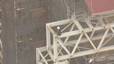 religion The person can be seen sitting high above the street on the construction site.