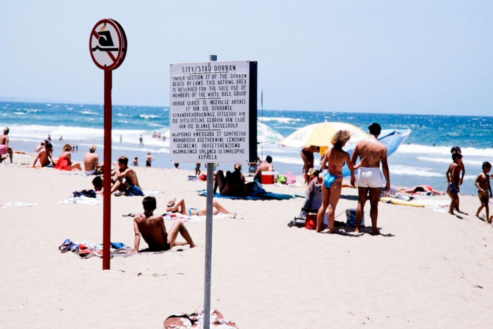 PHOTO: People swim and sunbathe near a notice board with the rules under which blacks were barred from swimming at the "Whites Only" section at a beach in Durban, South Africa, Jan. 5, 1987.