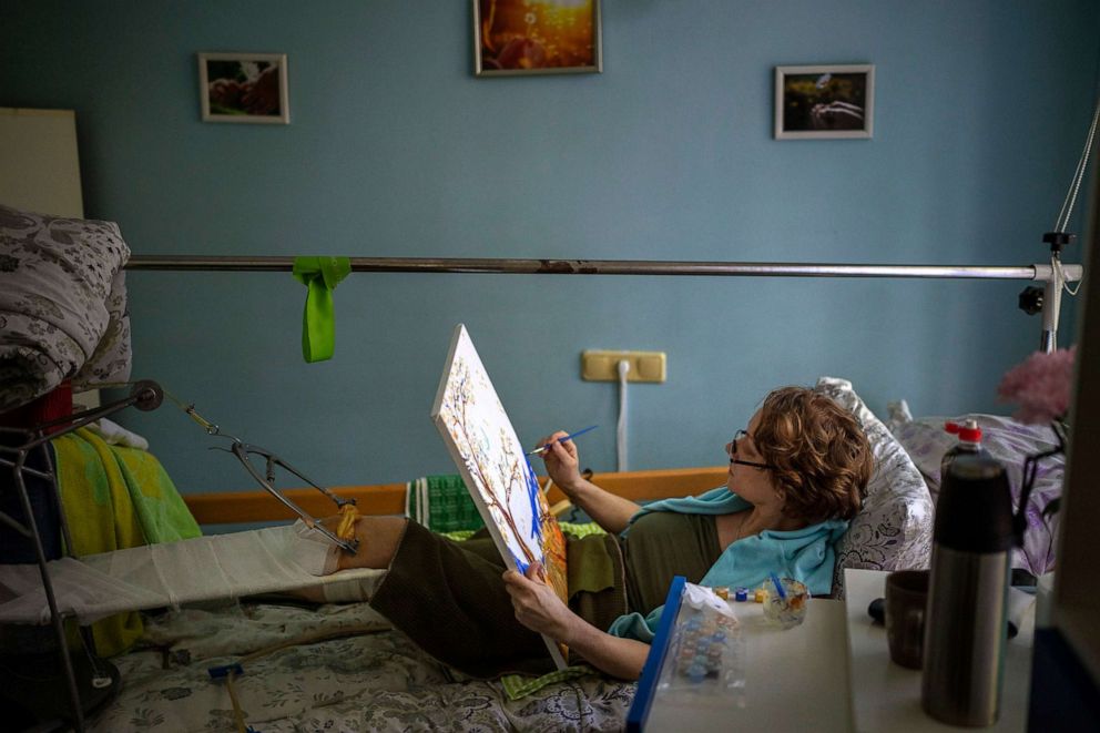 PHOTO: Olena Viter, 45, paints on her bed as she recovers from her wounds at a public hospital in Kyiv, Ukraine, May 10, 2022. Her son, 14-year-old Ivan, a budding musician already playing in a small orchestra, died, victim of the same explosion.