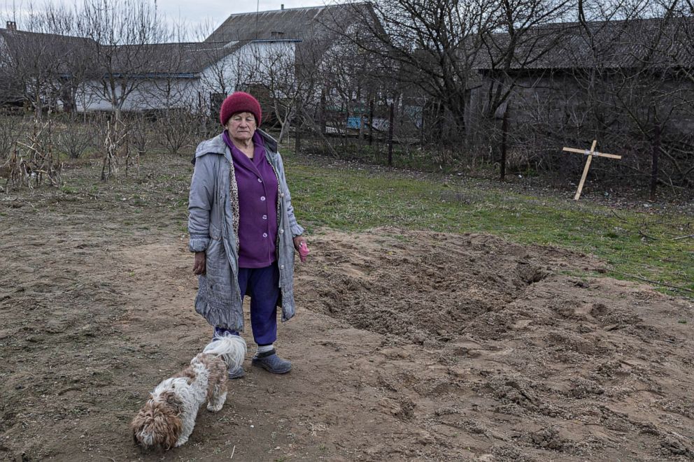 PHOTO: Tamara Klymchuk, 64, and her dog stand next to the grave of a man in the village. "We had a very good life." said Klymchuk.