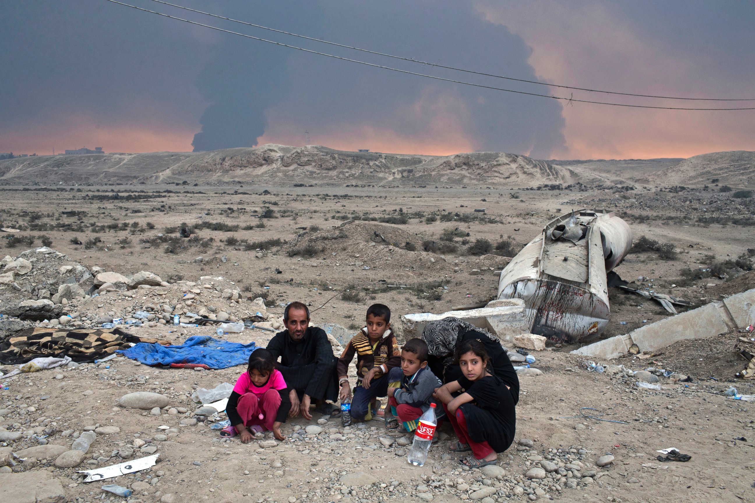 PHOTO: Internally displaced persons sit at a checkpoint as smoke rises from the burning oil wells in Qayyarah, about 31 miles (50 km) south of Mosul, Iraq, Oct. 23, 2016. 