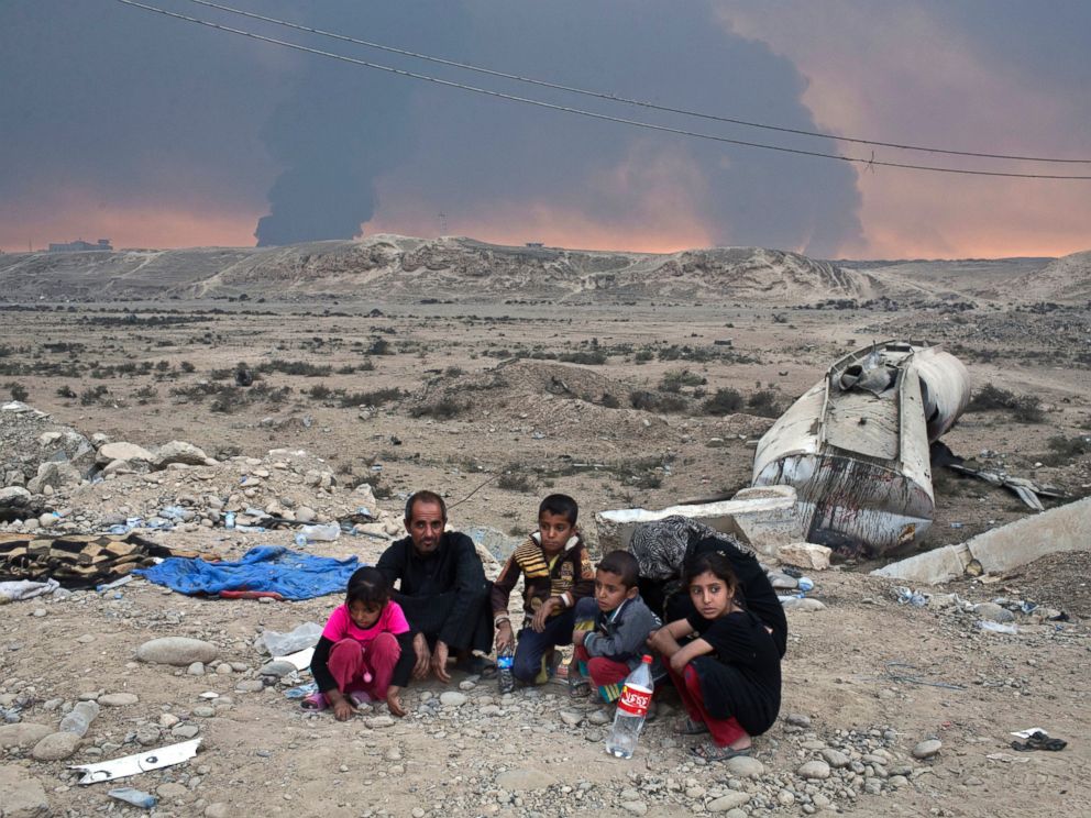 PHOTO: Internally displaced persons sit at a checkpoint as smoke rises from the burning oil wells in Qayyarah, about 31 miles (50 km) south of Mosul, Iraq, Oct. 23, 2016.
