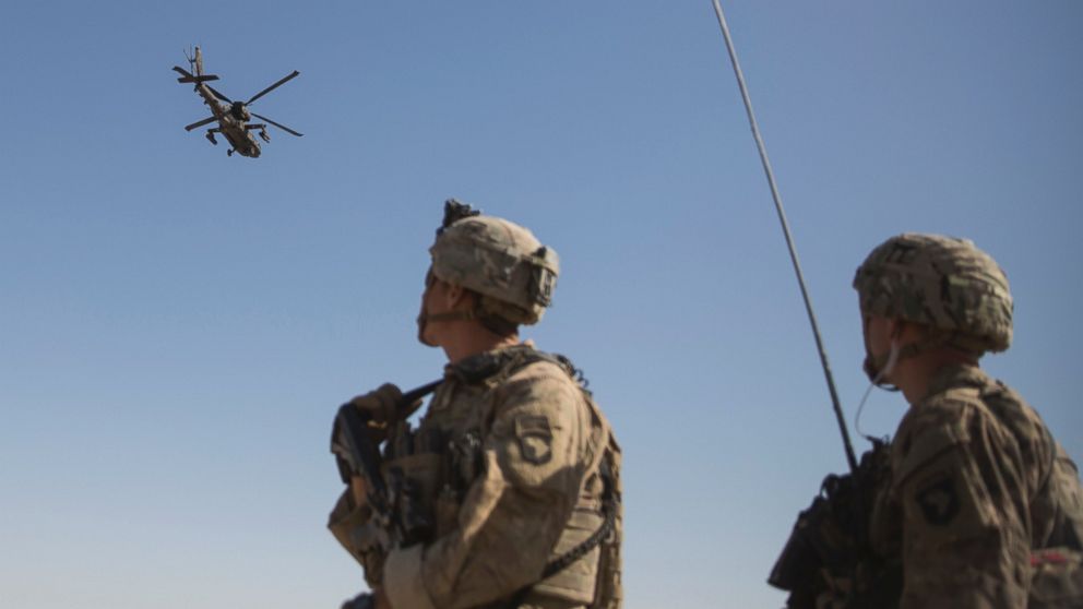 This June 10, 2017 photo released by the U.S. Marine Corpsshows an AH-64 Apache attack helicopter provides security from above while CH-47 Chinooks drop off supplies to U.S. Soldiers with Task Force Iron at Bost Airfield, Afghanistan.