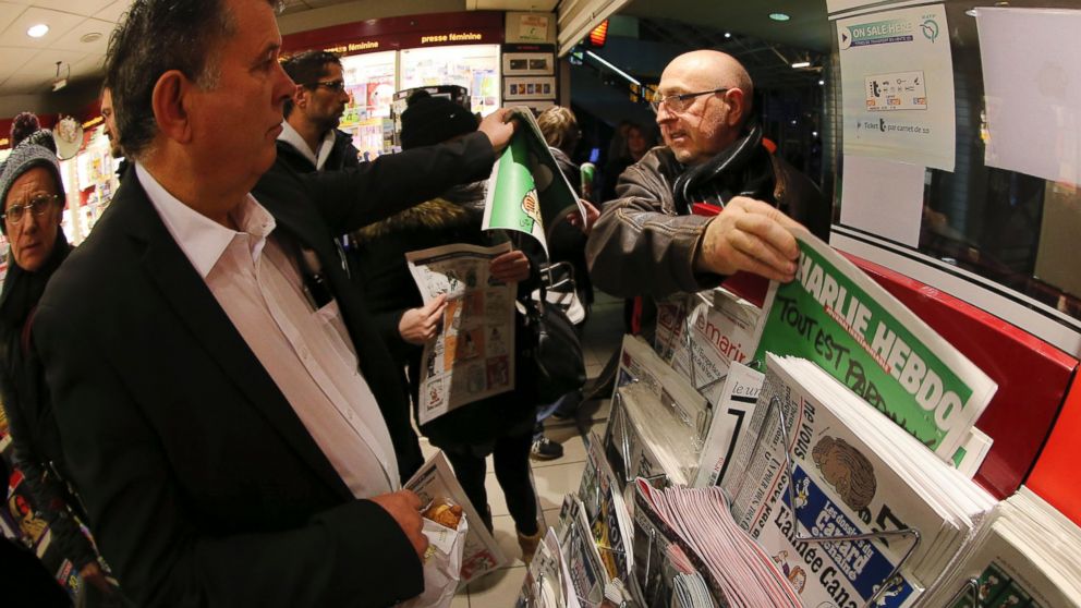 In this photo made with a fish-eye lens, people pick up copies of Charlie Hebdo newspaper at a newsstand in Rennes, western France, Jan. 14, 2015.
