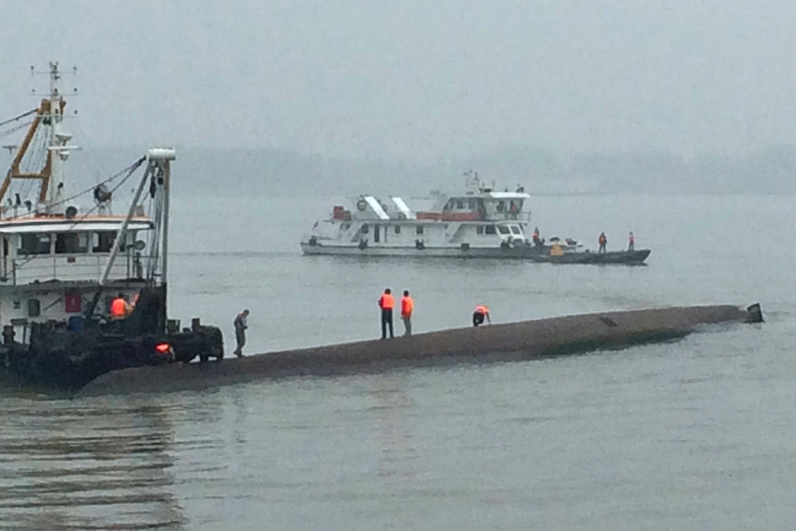 Rescue workers stand on the capsized ship, center, on the Yangtze River in central China's Hubei province June 2, 2015. The small cruise ship sank overnight in China's Yangtze River during a storm, leaving nearly 450 people missing, state media said.