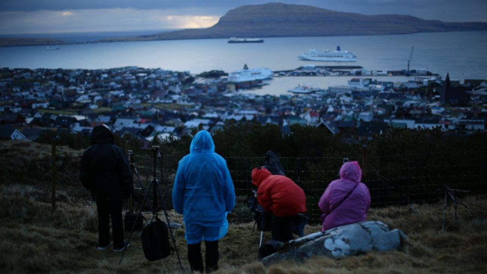 PHOTO: People wait for the start of a total solar eclipse on a hill beside a hotel overlooking the sea and Torshavn, the capital city of the Faeroe Islands, March 20, 2015.