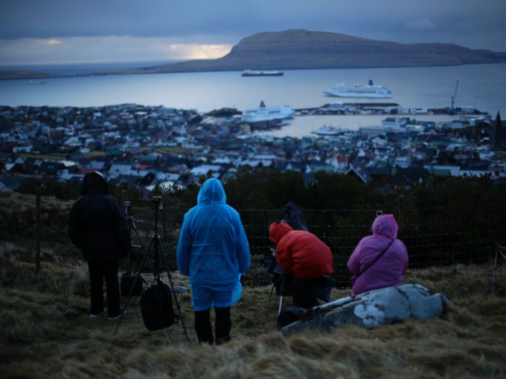 PHOTO: People wait for the start of a total solar eclipse on a hill beside a hotel overlooking the sea and Torshavn, the capital city of the Faeroe Islands, March 20, 2015.