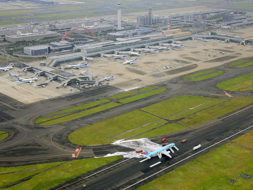 PHOTO: White form sprayed over the left engine of a Korean Air jet is seen after firefighters battled an apparent engine fire on the tarmac as passengers and crew members, bottom right, huddle on a grassy area at Haneda Airport in Tokyo May 27, 2016.