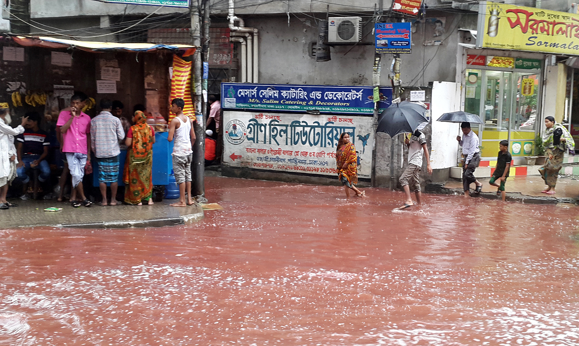 PHOTO: People wade past a road turned red after blood from sacrificial animals on Eid al-Adha mixed with water from heavy rainfall in Dhaka, Bangladesh. 