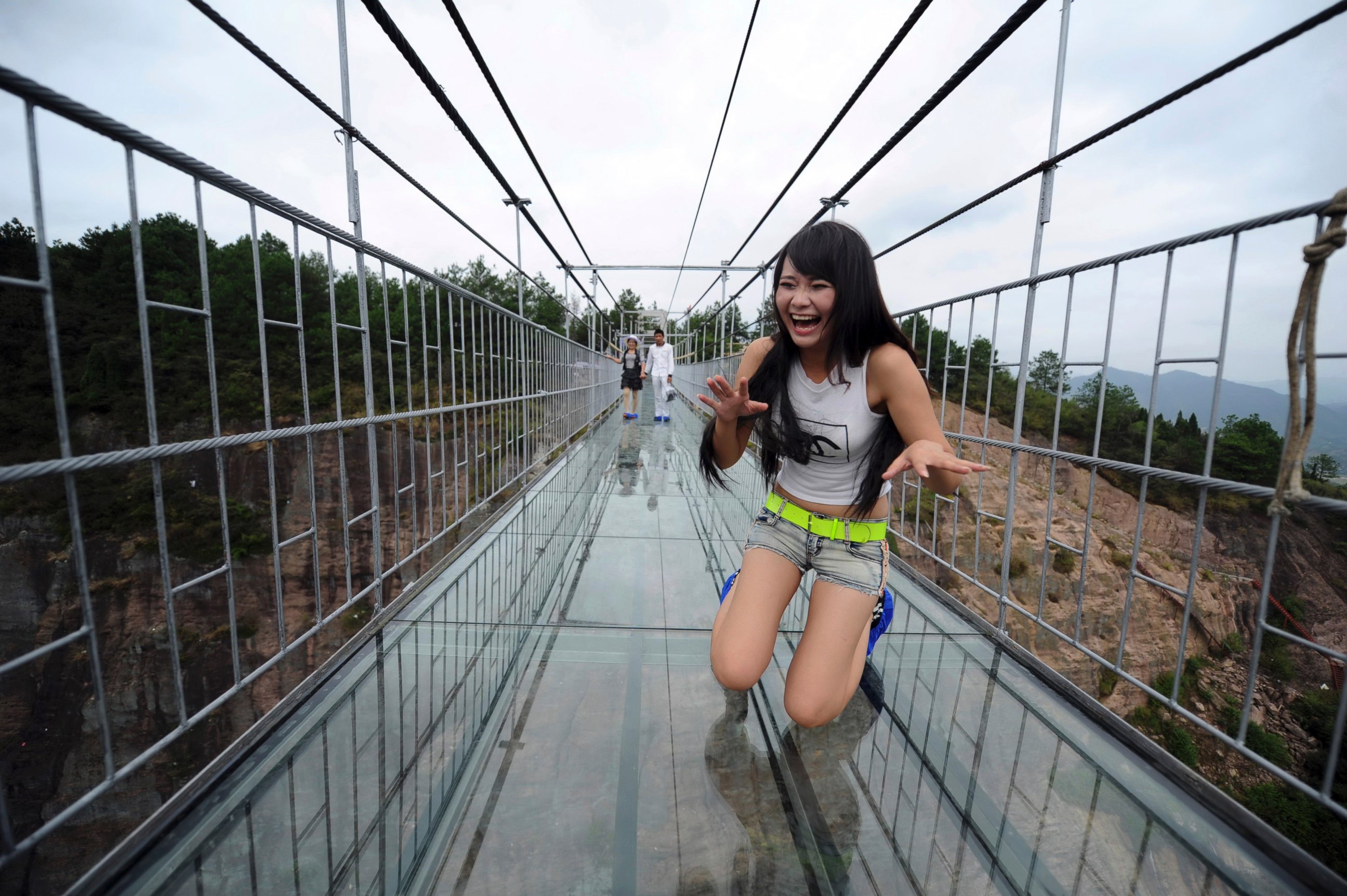 PHOTO: A woman plays around as she walks across a glass-bottomed suspension bridge in a scenic zone in Pingjiang county in southern China's Hunan province, Sept. 24, 2015. 