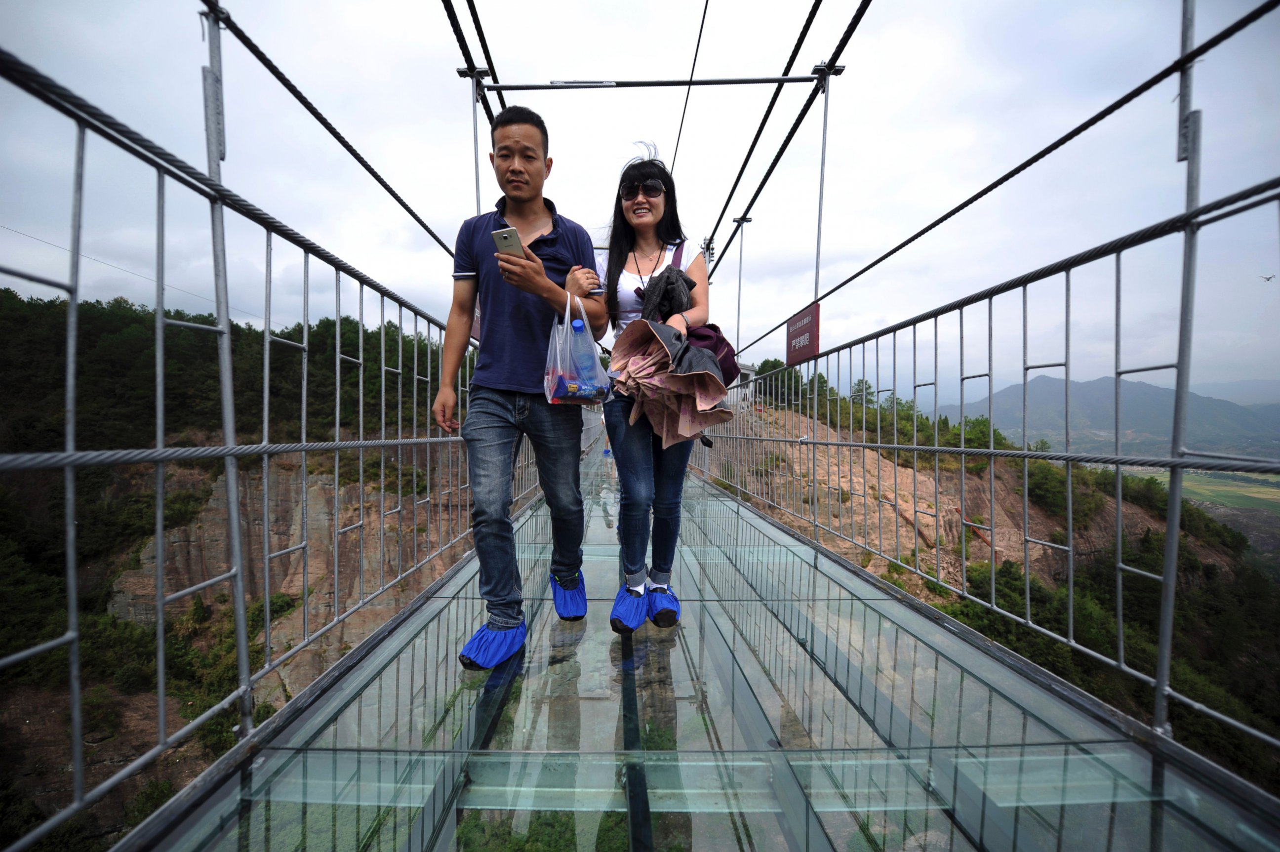 PHOTO: Visitors wear protective shoe coverings as they walk across a glass-bottomed suspension bridge in a scenic zone in Pingjiang county in southern China's Hunan province, Sept. 24, 2015. 