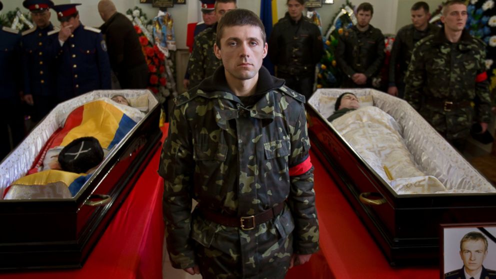 A Ukrainian soldier looks up standing between the coffins of Ukrainian soldier Sergey Kokurin, 35, right, and Russian Cossack militiaman Ruslan Kazakov, 34, left, during their funeral in Simferopol, Crimea, Saturday, March 22, 2014.