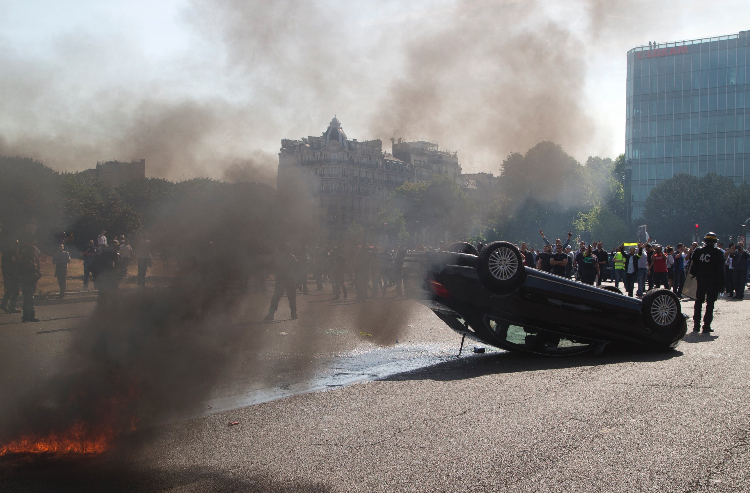 PHOTO: Striking taxi drivers stand behind an overthrown car during a taxi drivers demonstration, June 25, 2015, in Paris.