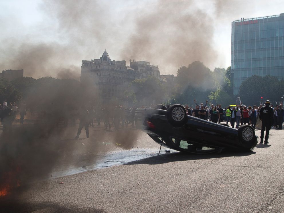 PHOTO: Striking taxi drivers stand behind an overthrown car during a taxi drivers demonstration, June 25, 2015, in Paris.