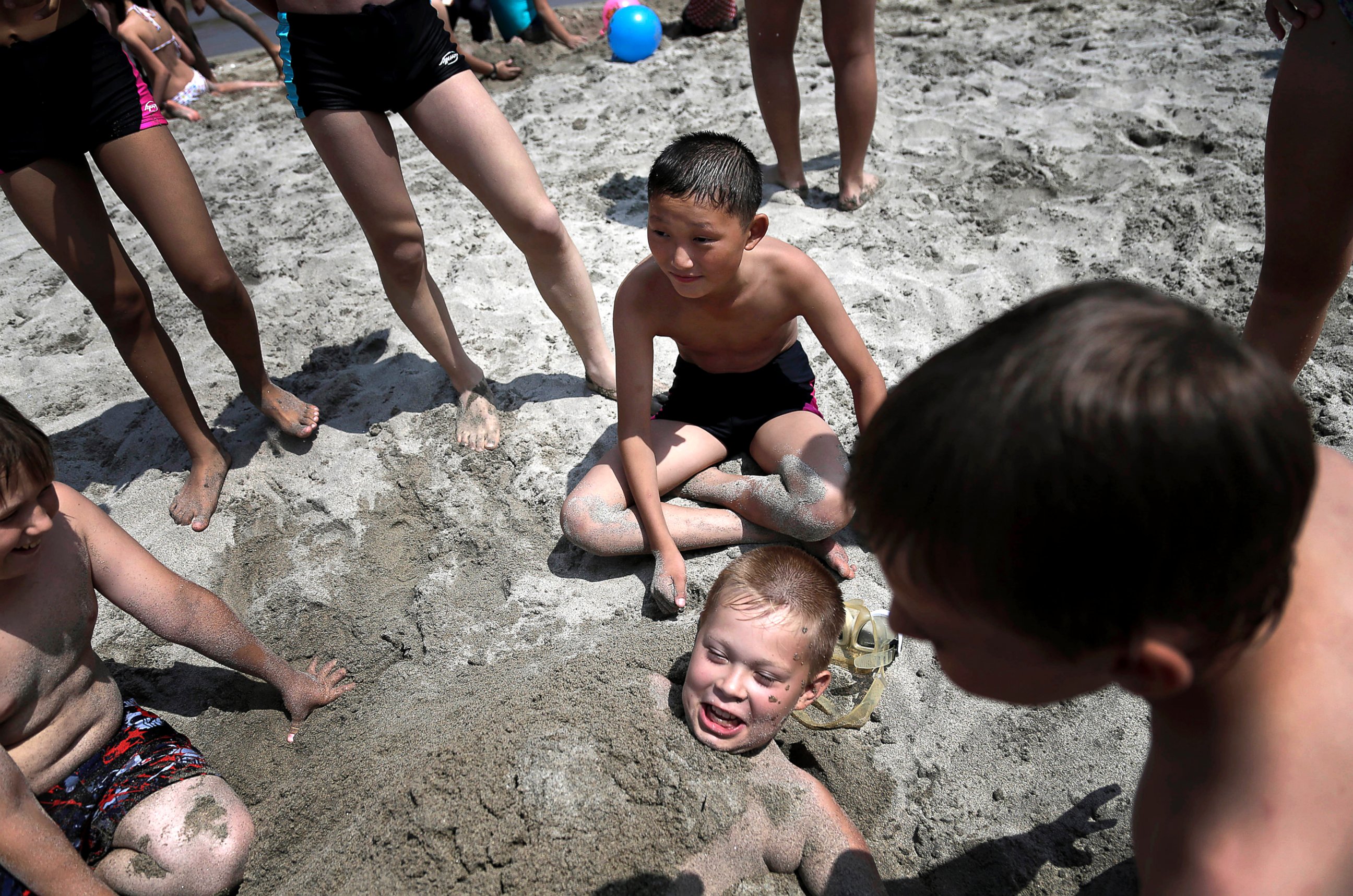 PHOTO: Kim Sun Gun, 12, of North Korea, center, smiles as he watches other students bury Russian student Konstantin Kostya, 10, in the sand at the Songdowon International Children's Camp, July 29, 2014, in Wonsan, North Korea.