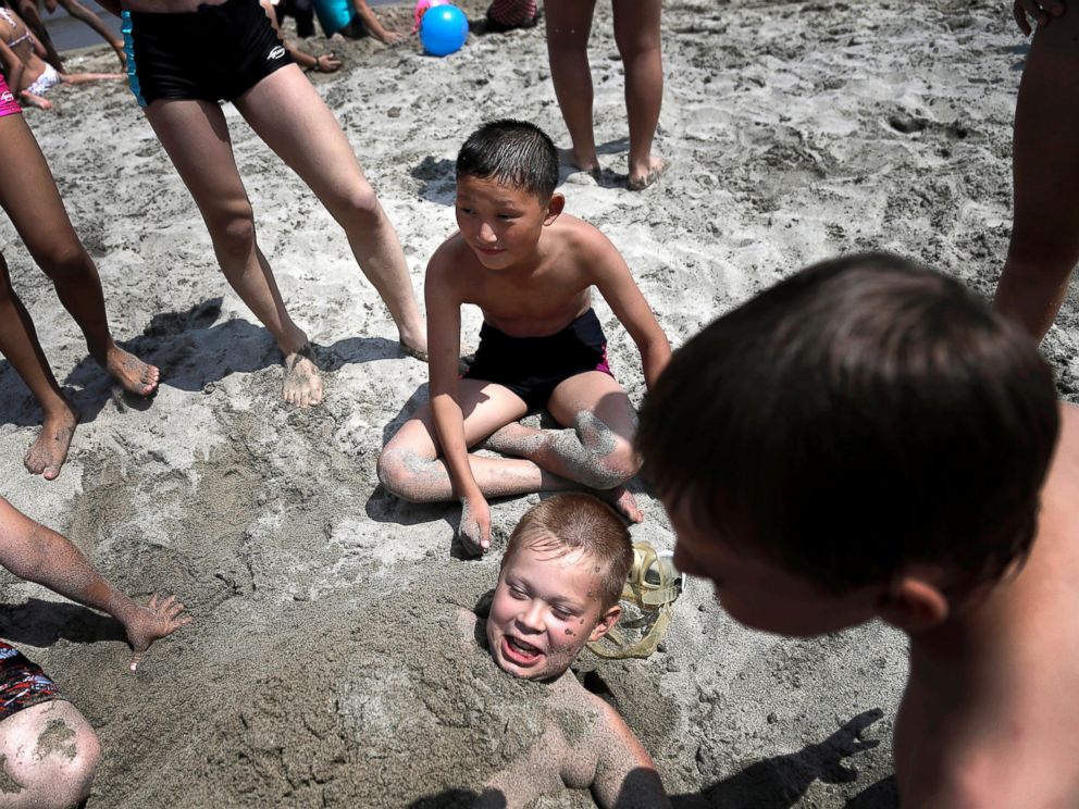 PHOTO: Kim Sun Gun, 12, of North Korea, center, smiles as he watches other students bury Russian student Konstantin Kostya, 10, in the sand at the Songdowon International Childrens Camp, July 29, 2014, in Wonsan, North Korea.