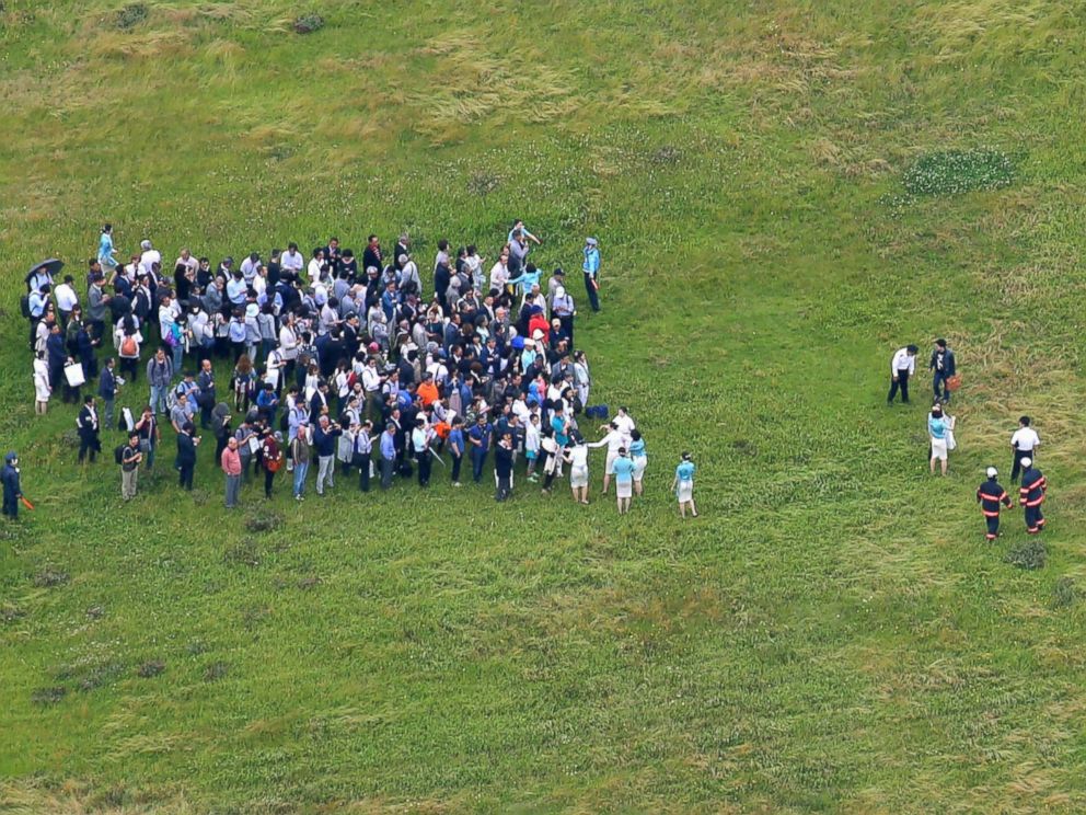 PHOTO: Passengers who escaped from a Korean Air jet gather on the grass-covered ground by the tarmac as firefighters battle an apparent engine fire at Haneda Airport in Tokyo May 27, 2016.