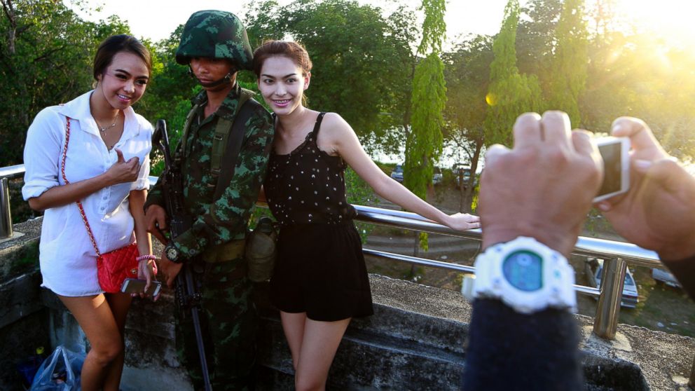 Passersby have their photograph taken with a Thai soldier guarding a pedestrian overfly near the site where pro-government demonstrators stage a rally on the outskirts of Bangkok, May 20, 2014. 