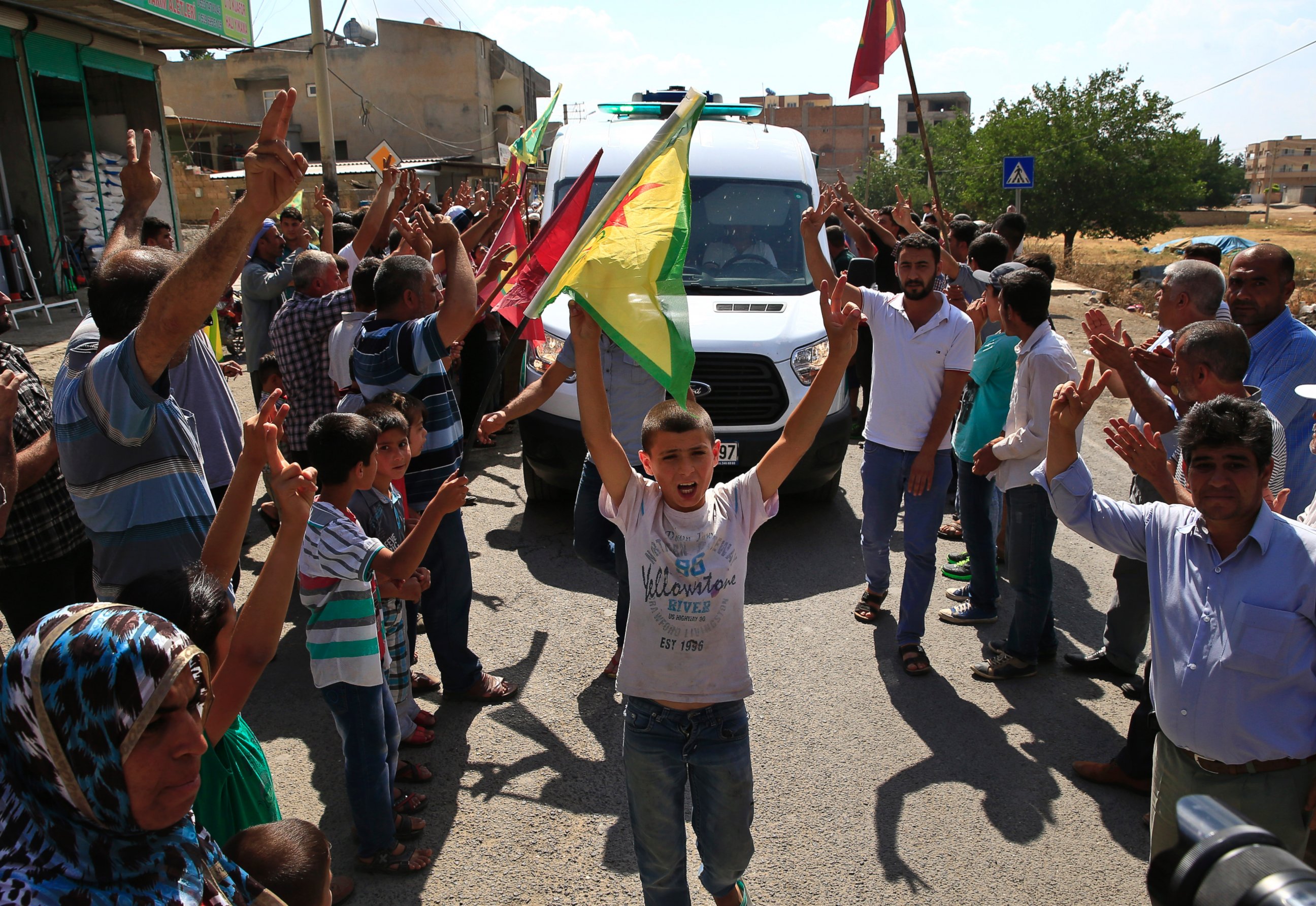 PHOTO: Kurdish people waving flags flash the V-sign and applaud while lining the road, as the convoy carrying the body of US citizen, Keith Broomfield.